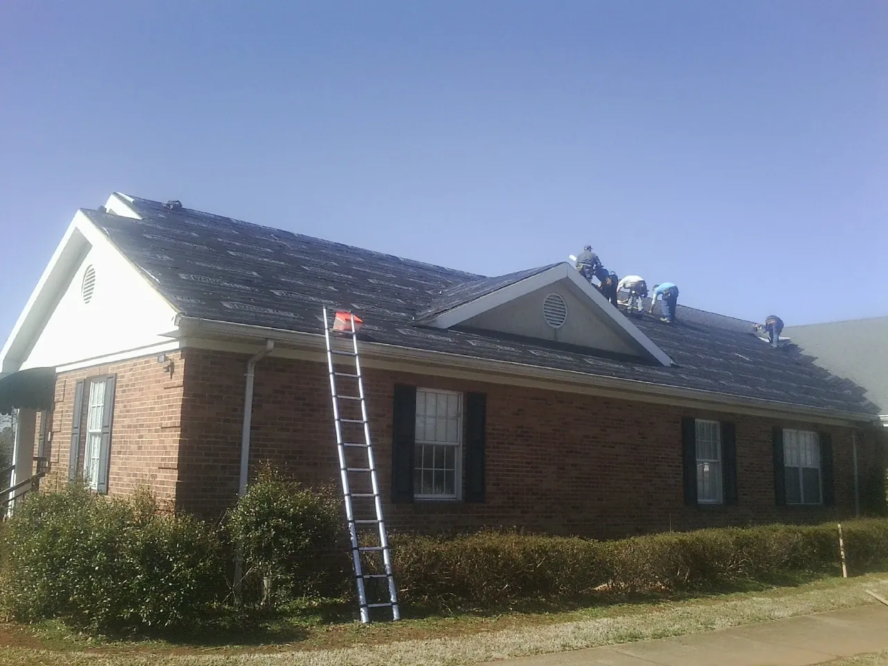 Crew tearing shingles off a brick ranch roof with a ladder set — Metal Roof Repair work by our crew in Echo