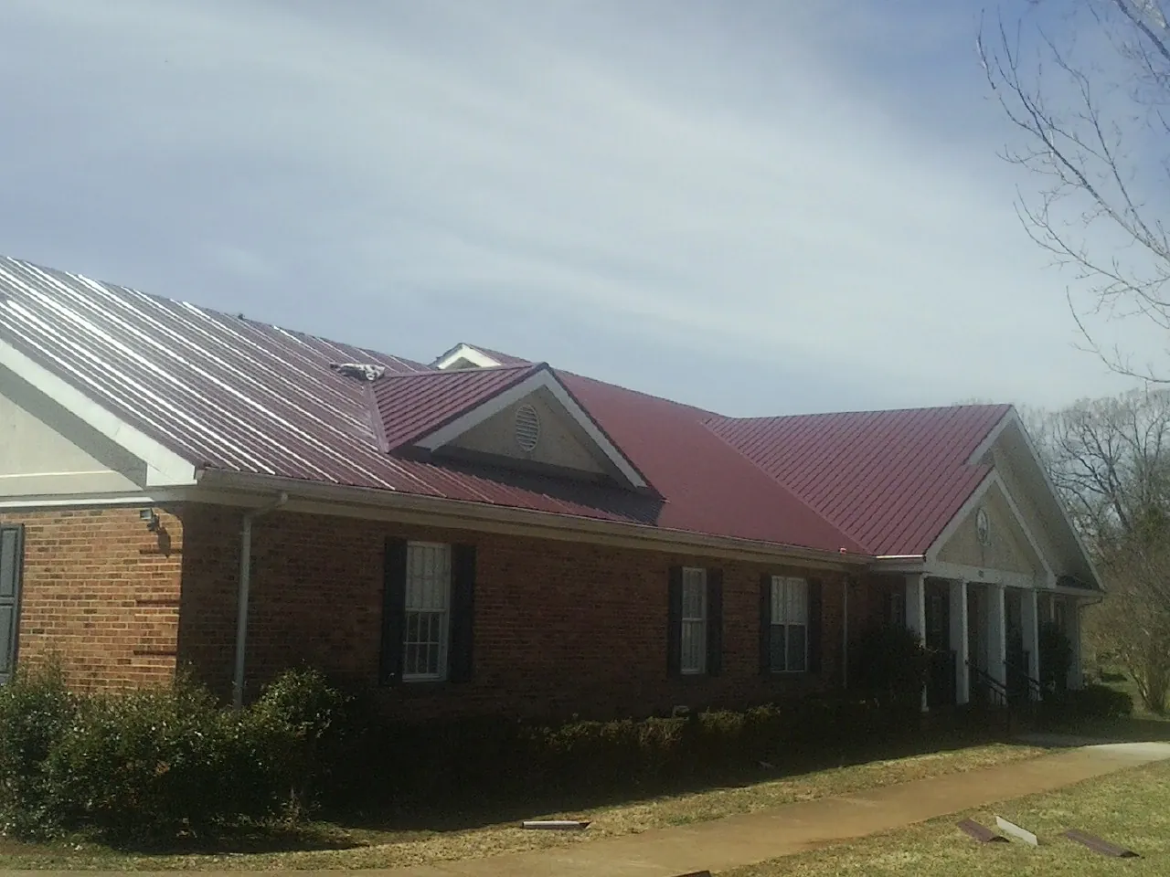 Red metal roof with gabled entries on a long brick building, from a Hail Damage Roof Repair job in Echo